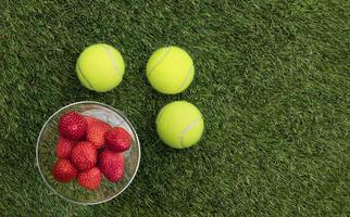 tenis pelotas y fresas en césped Disparo desde arriba. foto