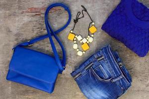 Women's autumn clothing and accessories blue sweater, jeans, handbag, beads on wooden background. photo