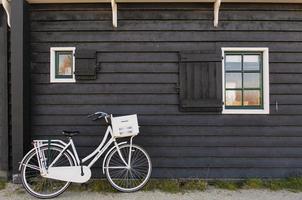 White bike parked against a wall made of dark wood. photo