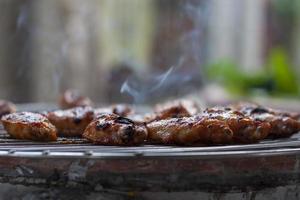 A la parrilla pollo alas en el parrilla con fumar iluminado flotante en el Clásico cocina. foto