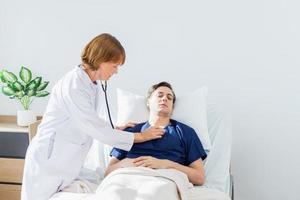 el médico es examinando el paciente en el hospital. caucásico hembra médico hablando a masculino paciente acostado en hospital cama. foto