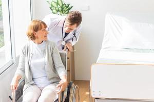 caucasian man doctor is examining the female older patient in wheelchair the hospital. photo