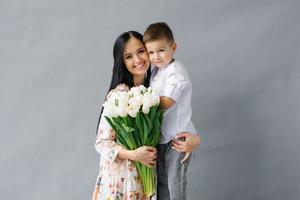 Portrait of a young mother with a bouquet of white tulips and a young son having fun. Family, charming child, the concept of love and happiness photo