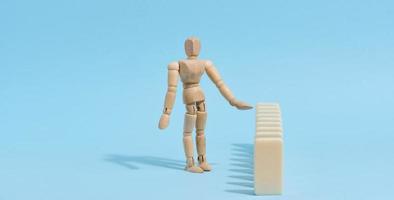 Wooden toy mannequin keeps dominoes from falling, risk prevention concept photo