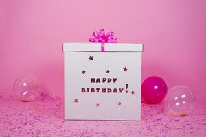 Big cardboard box birthday surprise and balloons with confetti on pink background photo