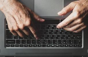 Hands of an elderly man learning to use computer, typing on a laptop, view from above photo