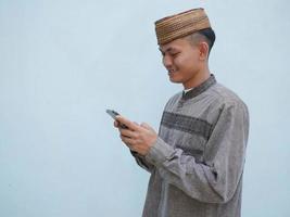 retrato de joven asiático musulmán hombre utilizando teléfono inteligente con contento expresión foto