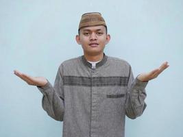 Young asian muslim man with surprised expression raises both hands photo