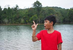 The boy smiled and pointed his hand to his side. On the background is a reservoir. photo