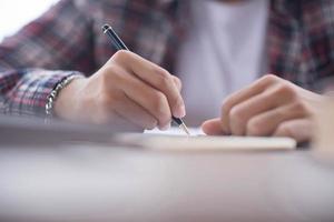 un negocio hombre es tomando notas dentro un cuaderno con un alarma reloj en el mesa. foto