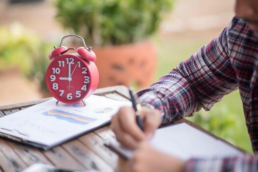 A business man is taking notes into a notebook with a telephone and an alarm clock on the table when the morning light. photo