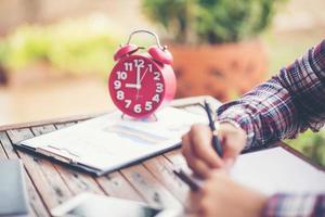 A business man is taking notes into a notebook with a telephone and an alarm clock on the table when the morning light. photo