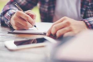 A business man is taking notes into a notebook with a telephone and an alarm clock on the table when the morning light. photo