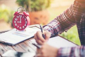 A business man is taking notes into a notebook with a telephone and an alarm clock on the table when the morning light. photo