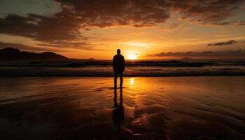 Photo of a sunset silhouette with a person standing on a beach at sunset.