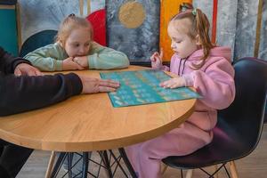 un familia con niños sentar en un café y estudiar el menú para ordenando alimento. foto