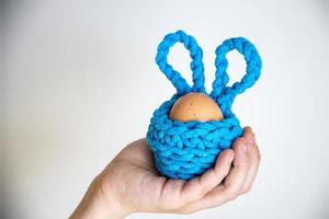 hand-made crochet turquoise Easter basket with eggs on a beige background kept in the hand of a child photo