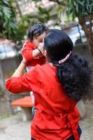 Loving mom carrying of her baby at society park. Bright portrait of happy mum holding child in her hands. Mother hugging her little 9 months old son. photo