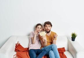 interesado hombre y mujer con palomitas de maiz en sofá naranja tartán y flor en un maceta foto