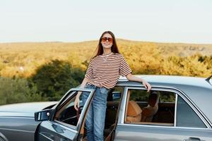 un joven mujer conductor mira fuera de el coche a el otoño paisaje y sonrisas satisfactoriamente foto