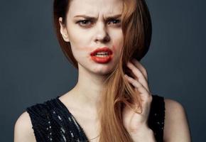 A woman in a black dress with red lips gestures with her hands puzzled look gray background photo