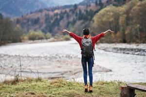 mujer caminante cerca el río con manos elevado arriba montañas paisaje foto