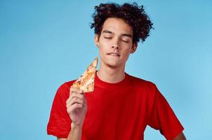 energético chico con un rebanada de Pizza teniendo divertido en un azul antecedentes y un rojo camiseta foto