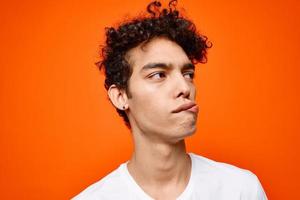 cute guy in white t-shirt curly hair grimace orange background photo