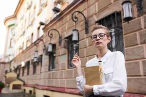 student with glasses walking around the city with a book education photo