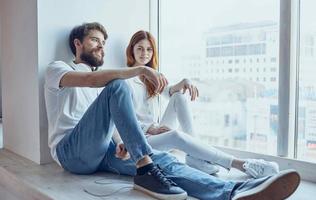 young couple in headphones sitting on the windowsill rest at home photo