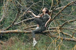 A woman in a green jumpsuit sits on a broken tree in sneakers photo