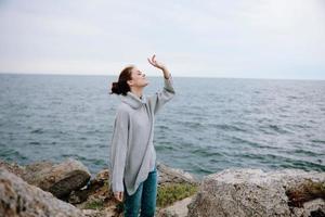 woman in a gray sweater stands on a rocky shore nature Relaxation concept photo