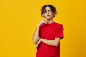 confuso gracioso caucásico joven hombre en rojo camiseta lata no hacer decisión posando aislado en terminado amarillo estudio antecedentes. el mejor oferta con gratis sitio para publicidad. emociones para todos los días concepto foto