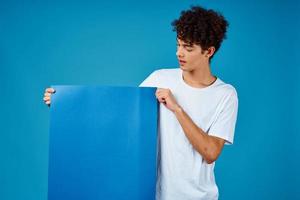 guy in a white t-shirt holding a poster mockup advertising blue background photo