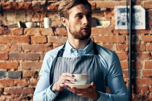 masculino camarero delantal café taza ladrillo pared restaurante Servicio foto