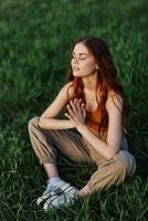 un joven mujer en verano ropa sentado en el verde césped haciendo yoga y meditando en naturaleza, un conexión con el cosmos. el concepto de armonía con cuerpo y naturaleza, espiritual crecimiento foto