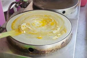 Cooking crepe dessert with topping with egg sale in street food market Thailand. photo