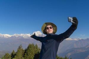 A young traveler takes a selfie or a video call while standing a top a mountain. photo