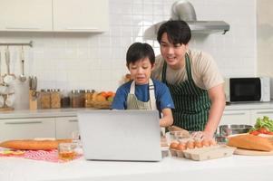 contento sonriente joven asiático padre y hijo haciendo vídeo llamada a madre. disfrutar Cocinando en cocina a hogar foto