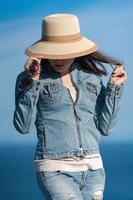 Portrait of female in denim jacket and jeans hiding with straw hat over his face photo