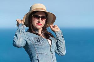 Caucasian ethnicity woman in sunglasses raised her hands and holding straw hat on her head photo