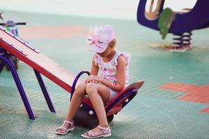 Sad girl sits alone on a swing in the playground. Outcast, loneliness. photo