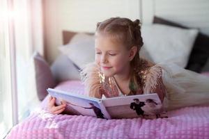 A little beautiful girl lies on the bed and looks at her parent is wedding photo album.