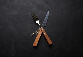 Fork and knife with wooden handle on black background, top view photo