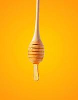Flowing drops of yellow honey from a wooden stick on a yellow background photo