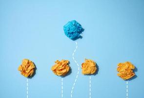 Crumpled paper balls on a blue background, one of them follows an individual path photo
