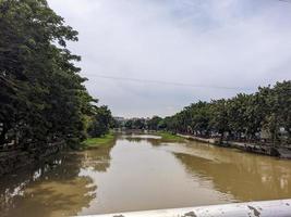 a view of brown river with blue sky and trees beside it in surabaya, indonesia photo