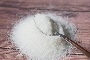 Sugar on spoon and wooden background, white sugar for food and sweets dessert candy heap of sweet sugar crystalline granulated photo