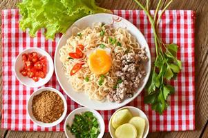 instant noodles cooking tasty eating with bowl - noodle soup, noodles bowl with boiled egg minced pork vegetable spring onion lemon lime lettuce celery and chili on table food photo