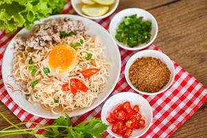 instant noodles cooking tasty eating with bowl - noodle soup, noodles bowl with boiled egg minced pork vegetable spring onion lemon lime lettuce celery and chili on table food photo